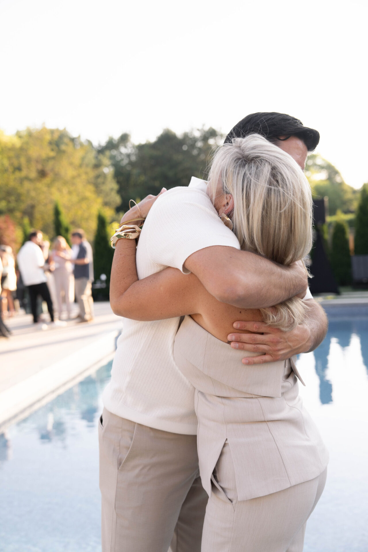 Two guests sharing a warm hug beside a pool during an outdoor celebration