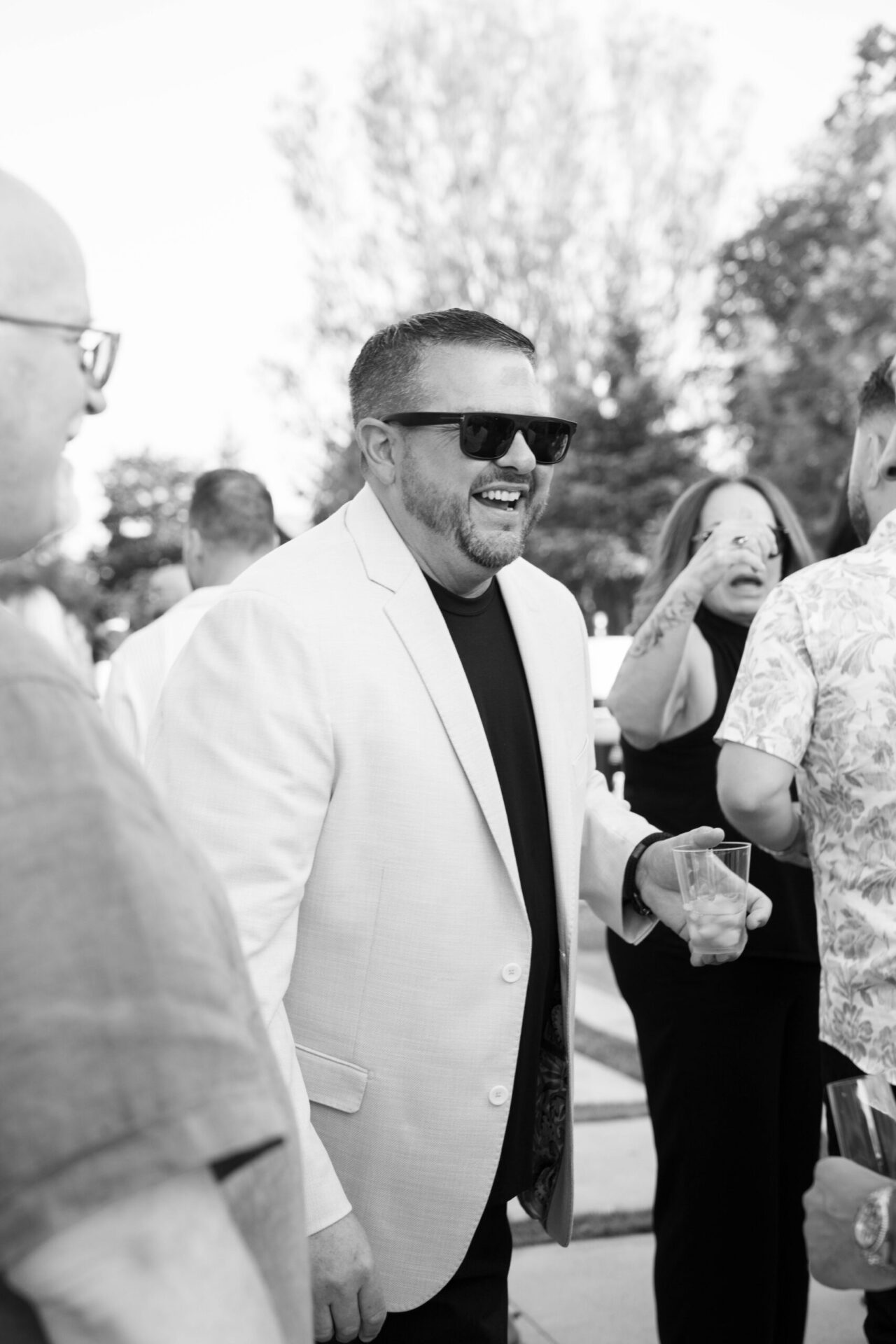 Black and white candid portrait of a smiling wedding guest wearing sunglasses