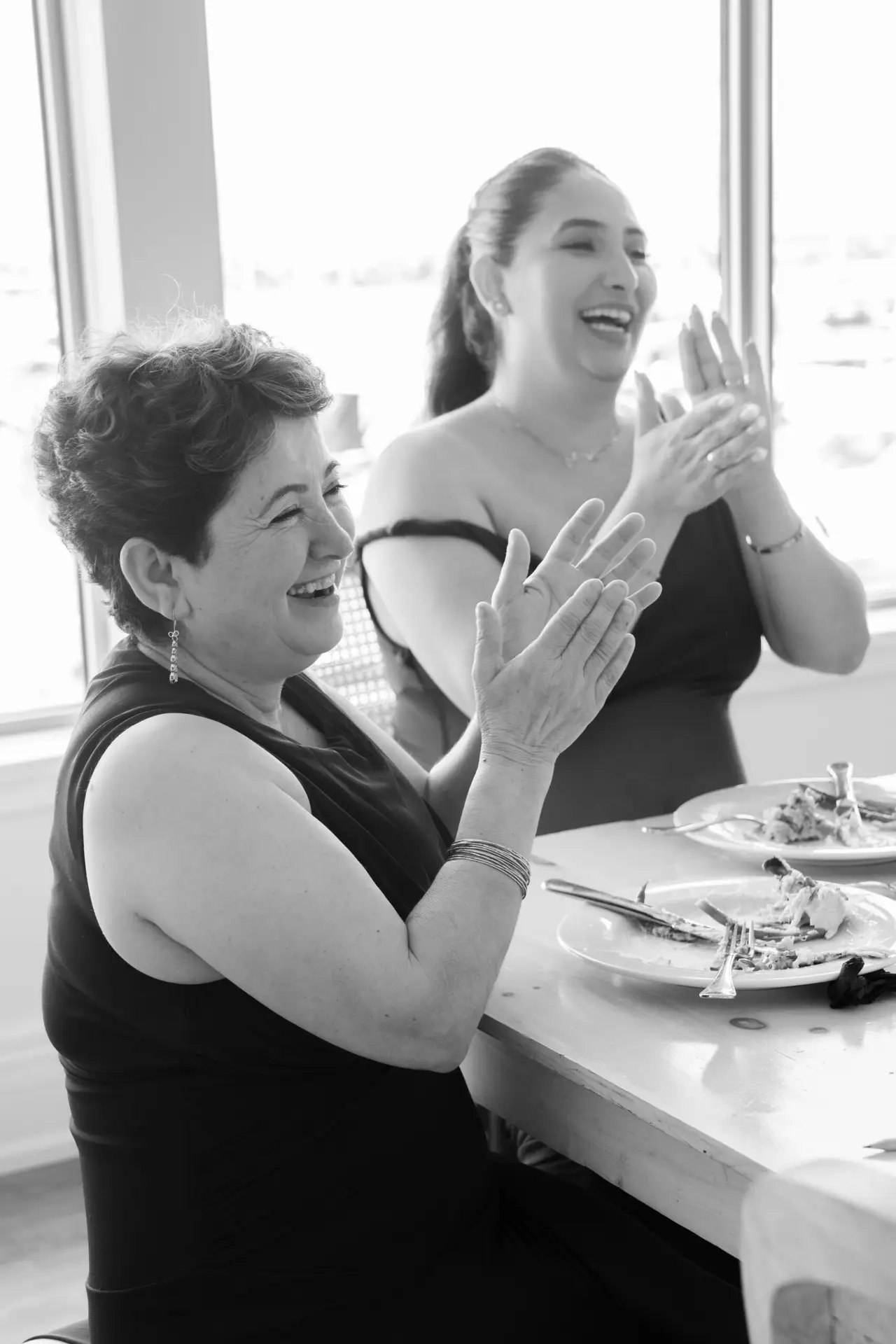 Black and white candid photo of guests laughing and talking around a table at an event